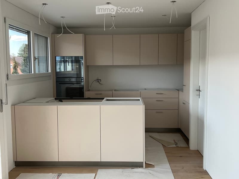 Empty kitchen with light-colored cabinets, a central island, and wooden flooring. No appliances or furniture are present.