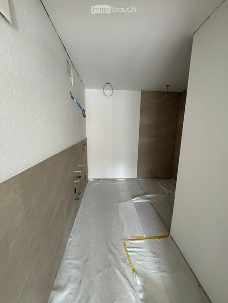 Empty room with bare walls and a protective plastic sheet on the floor, likely under renovation.