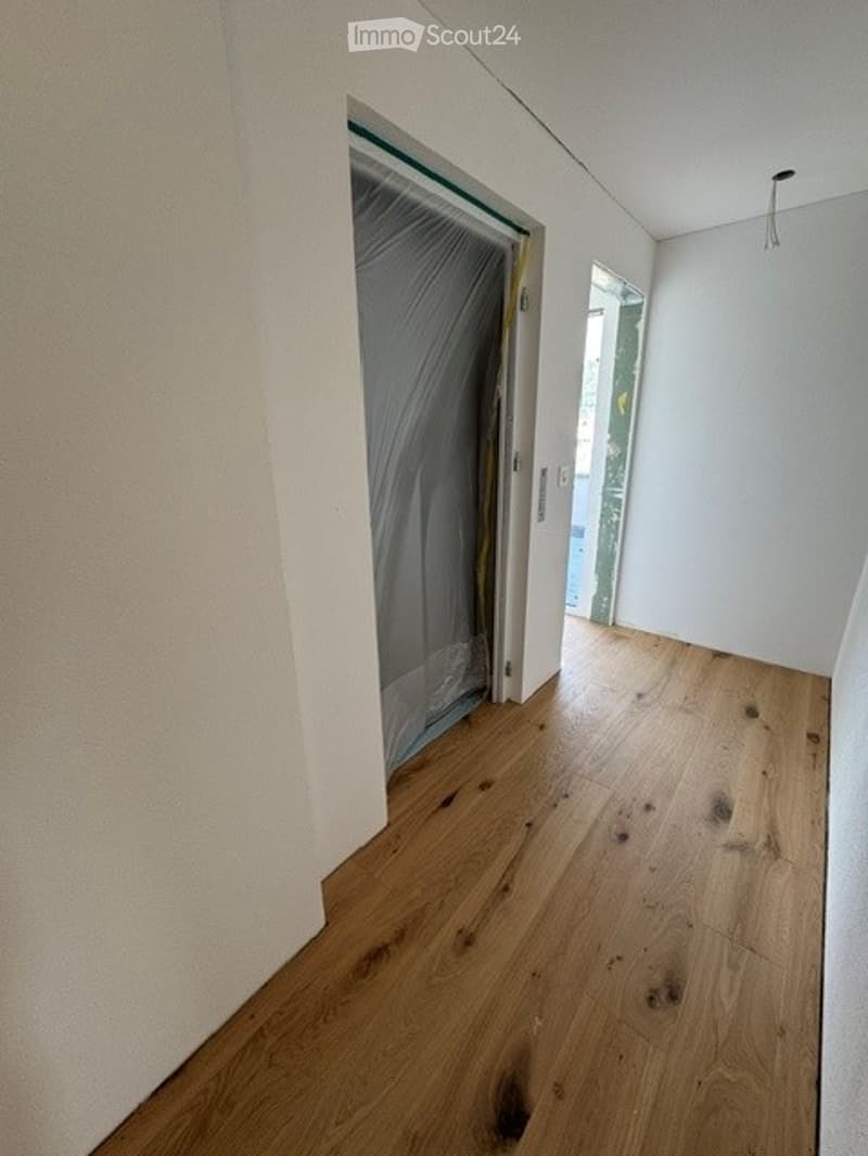 Empty room with wooden flooring and white walls, featuring a doorway leading to another space.