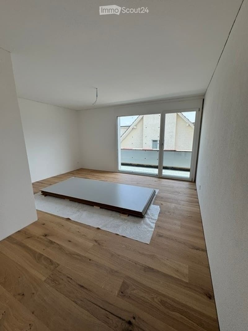 Empty room with wooden flooring, white walls, and a large sliding glass door leading to a balcony.