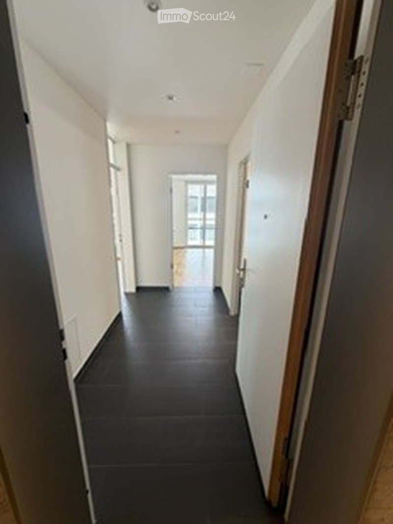 Empty hallway with dark tiled floor, white walls, and several doors leading to rooms.