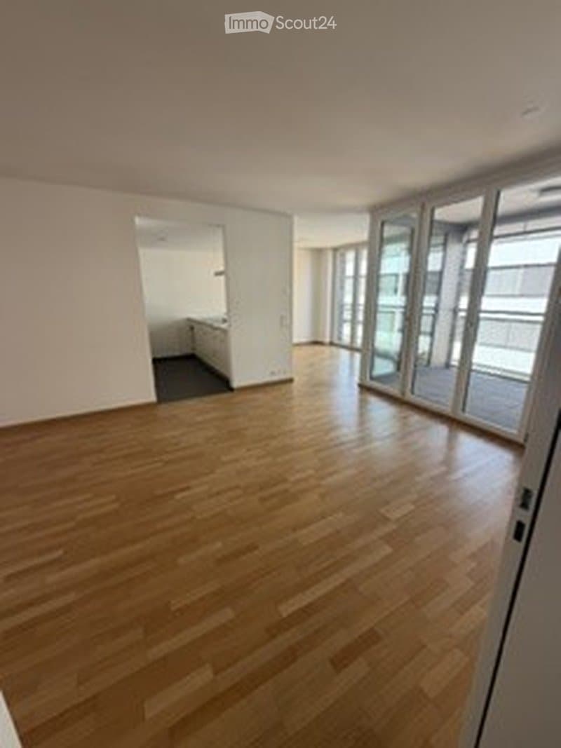 Empty room with wooden flooring, large glass sliding doors leading to a balcony, and a doorway to another room.