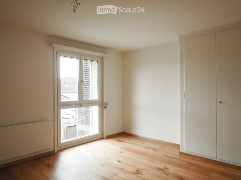 Empty room with wooden flooring, white walls, and a large window with a view of the outside.