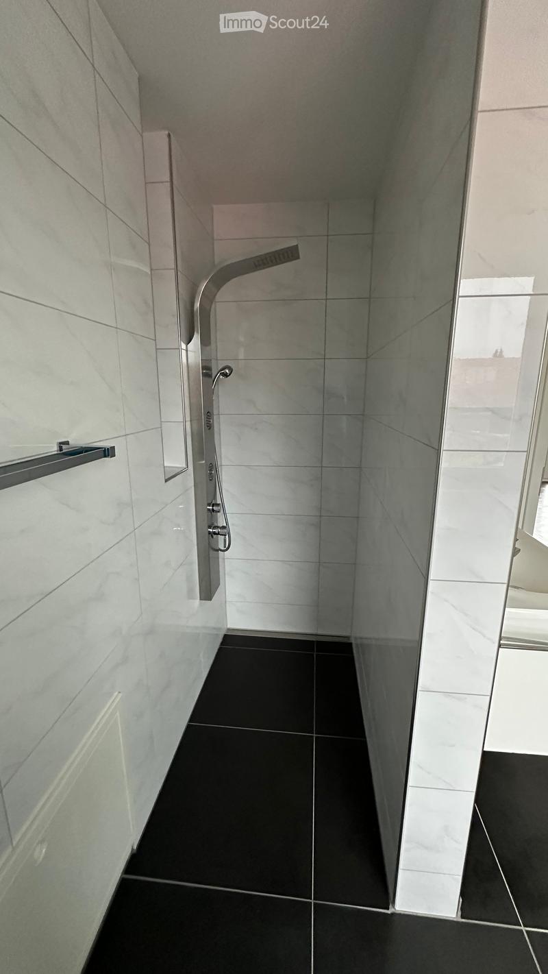 Modern bathroom with white marble tiles, black floor tiles, and a glass-enclosed shower area featuring a modern shower handle and rail.