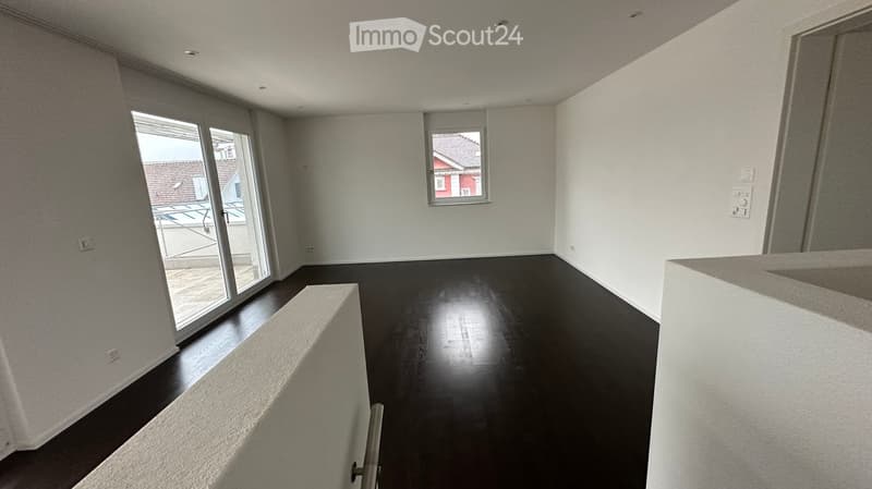 Empty room with dark wooden flooring, white walls, large sliding glass door, and a small window showing a view of the outside.