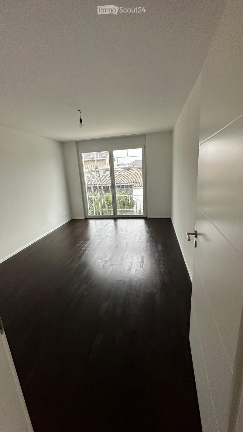 Empty room with dark wooden flooring, white walls, and a large sliding glass door leading to a balcony.
