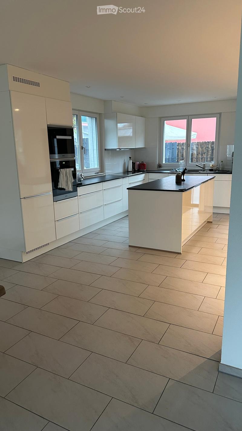 Modern kitchen with white cabinets, a central island, and tiled flooring. Features include a built-in oven, refrigerator, and sink with a window above.
