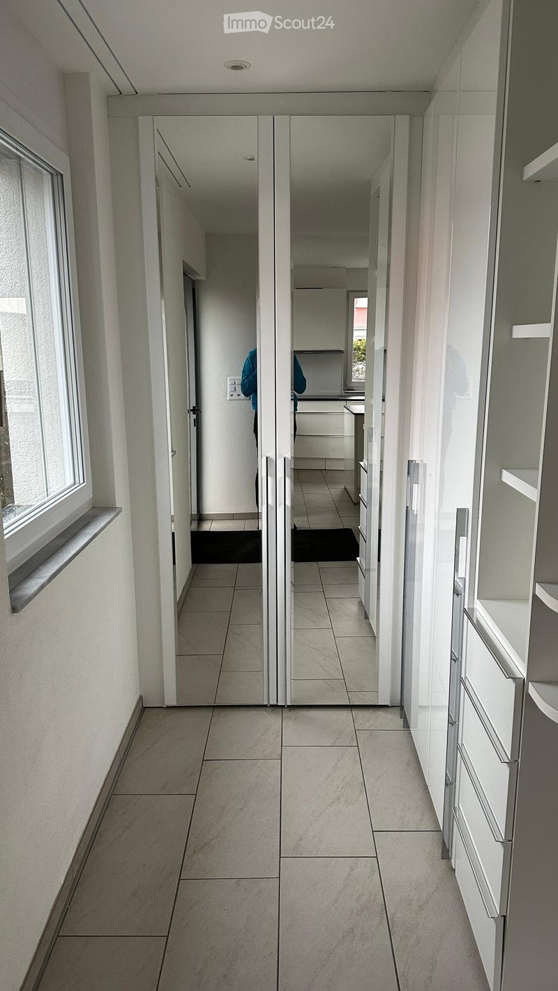 Modern hallway with tiled flooring, white walls, large windows, and mirrored doors leading to a kitchen area.