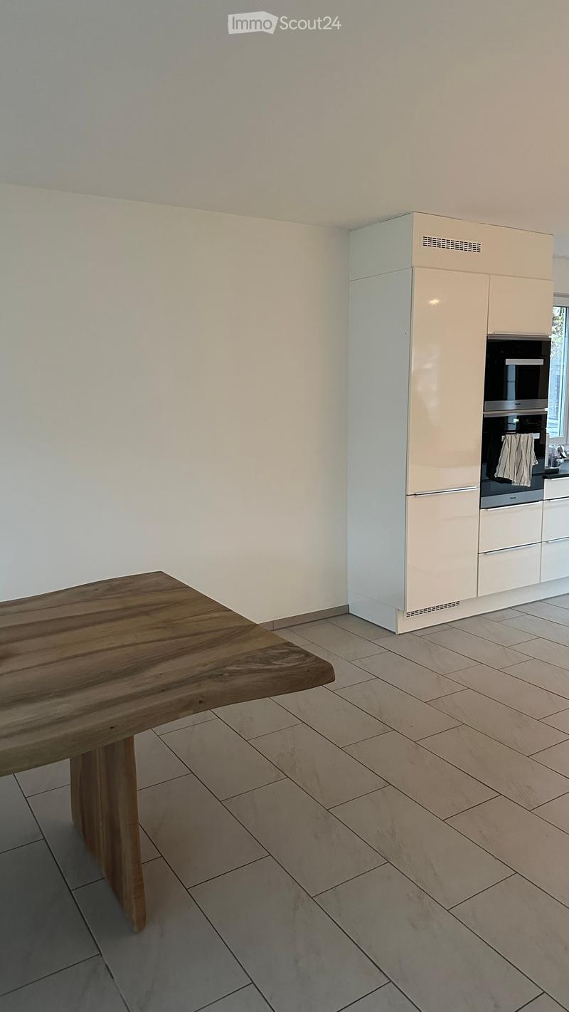 Modern kitchen with light-colored cabinets, a wooden table, and tiled flooring.