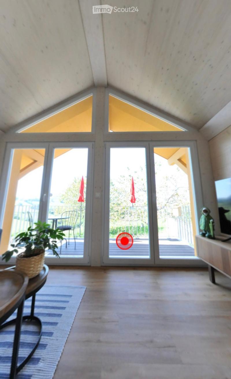 Bright living space with large glass doors leading to a balcony, featuring a small table, chair, potted plant, and a screen on a wooden stand.