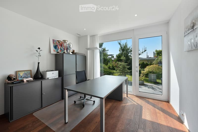 Modern office space with a large glass door leading to a garden, featuring a sleek office table, ergonomic chair, and grey cabinetry.