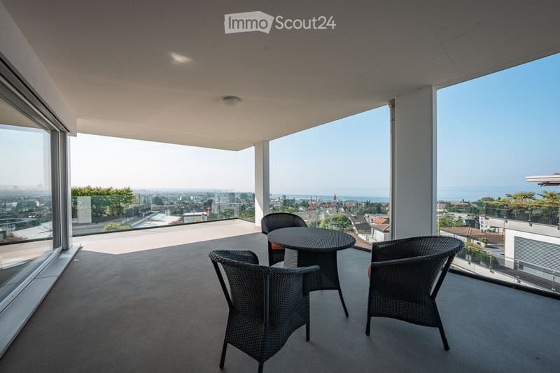 Modern balcony with panoramic city and sea views, featuring a round table and four wicker chairs.