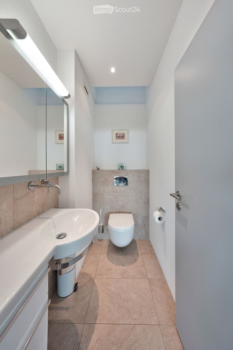 Modern bathroom with a white sink, toilet, and mirror. Light-colored tiles and sleek fixtures.