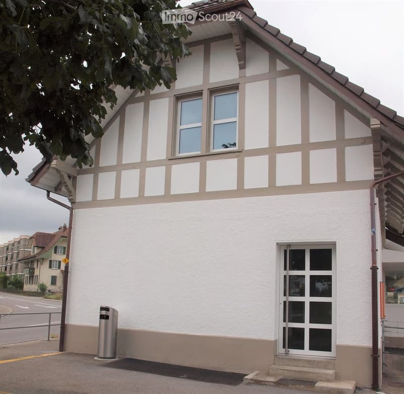 Two-story building with white walls, large windows, and a raised ground floor entrance.