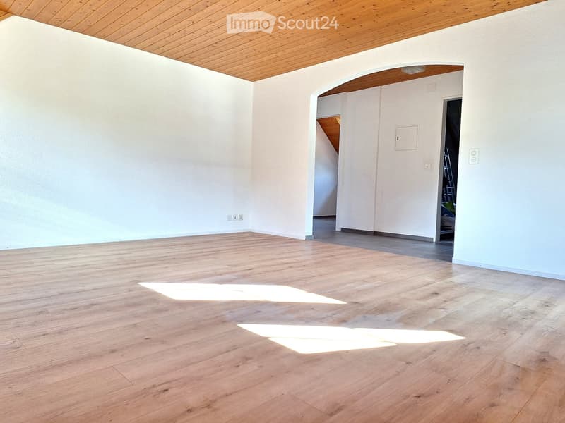 Large room with white walls, wooden floor, archway, entrance to another room with an attic