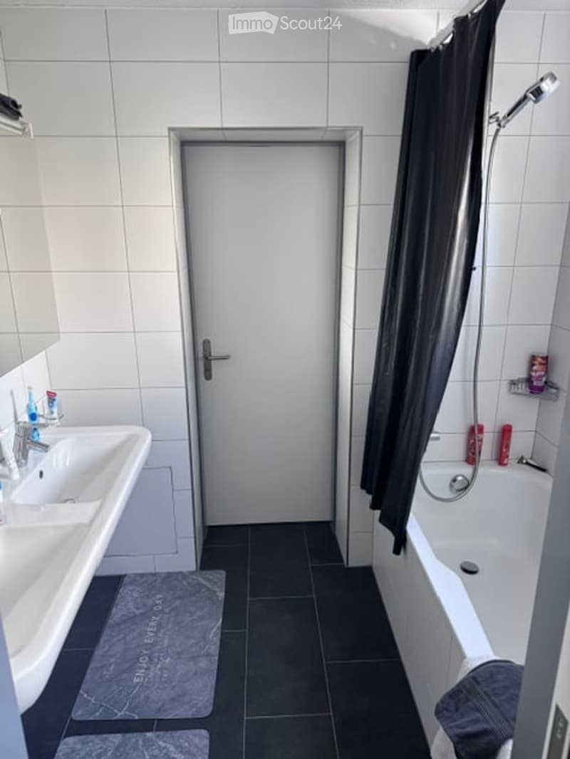 Modern bathroom with white tiled walls, black tiled floor, double sink, bathtub with shower, and a black shower curtain.