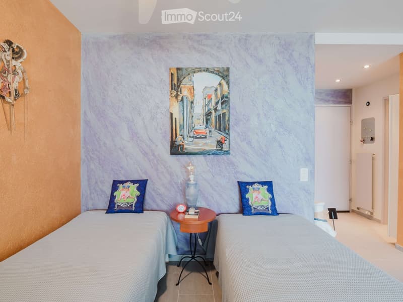 Cozy bedroom with two single beds, a small round table between them, decorative pillows, a vase, and a painting on the wall.