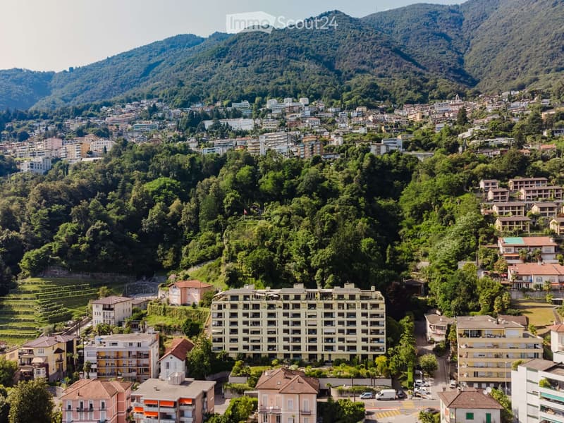 Aerial view of a town nestled in a lush, green valley surrounded by mountains. The town features a mix of residential and commercial buildings, with many multi-story structures and smaller houses scattered across the landscape. The area is densely populat