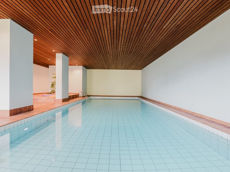 Indoor swimming pool area with wooden ceiling, tiled pool, and surrounding walls.