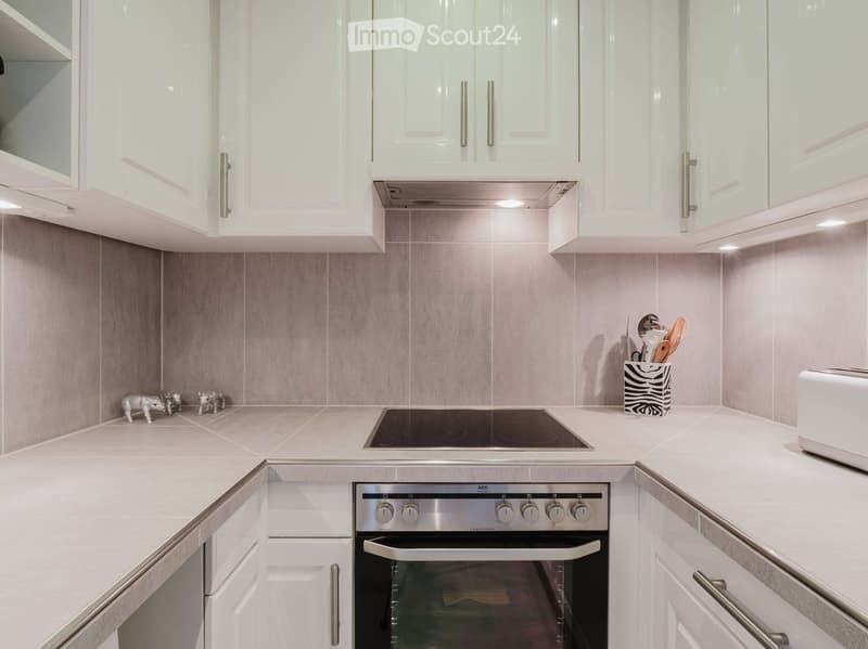 Modern kitchen with white cabinets, stainless steel oven, induction cooktop, and countertop with small decorative items and utensils.