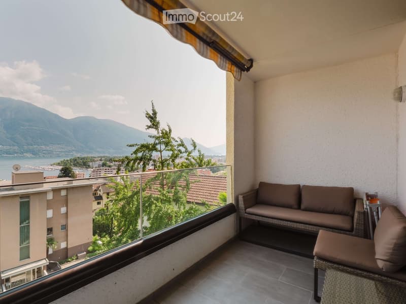 Balcony with a view of mountains and a lake, featuring a sofa and a chair.