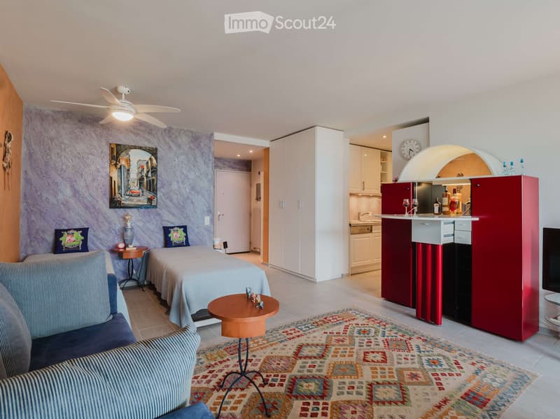 A modern, open-concept living and bedroom space with a sofa, coffee table, bed, nightstand, bar cabinet, and decorative items.