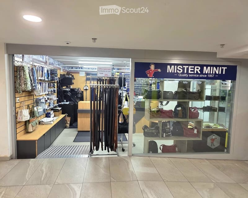 Storefront of a retail shop with shelves displaying bags, belts, and clothing racks inside.