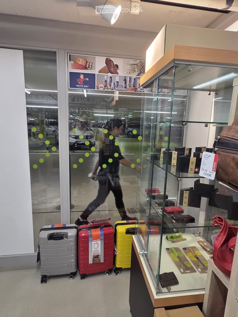Retail store display with suitcases, handbags, wallets, and accessories on a table inside a glass case.