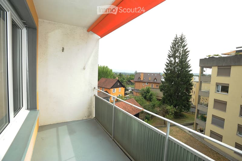 Balcony with metal railing, overlooking a residential area with houses, trees, and neighboring buildings.