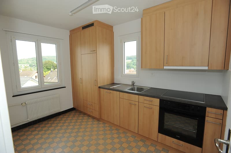 Modern kitchen with wooden cabinets, black countertop, sink, and built-in oven. Features checkered tile flooring and large windows offering a scenic view.
