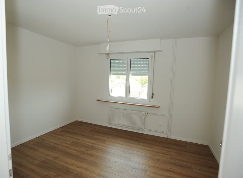 Empty room with wooden flooring, white walls, a window with blinds, a radiator, and a small shelf under the window.