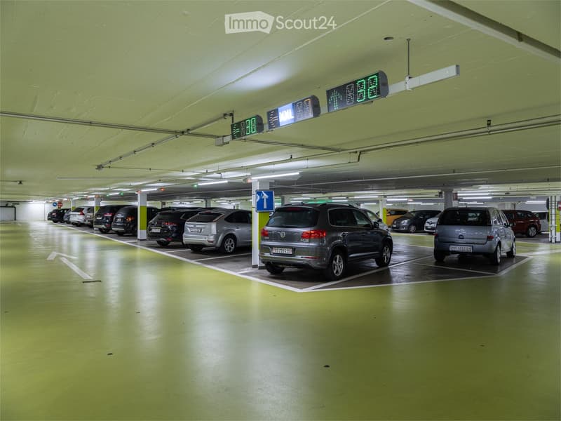 Underground parking lot with several parked cars, marked parking spaces, and directional signage.