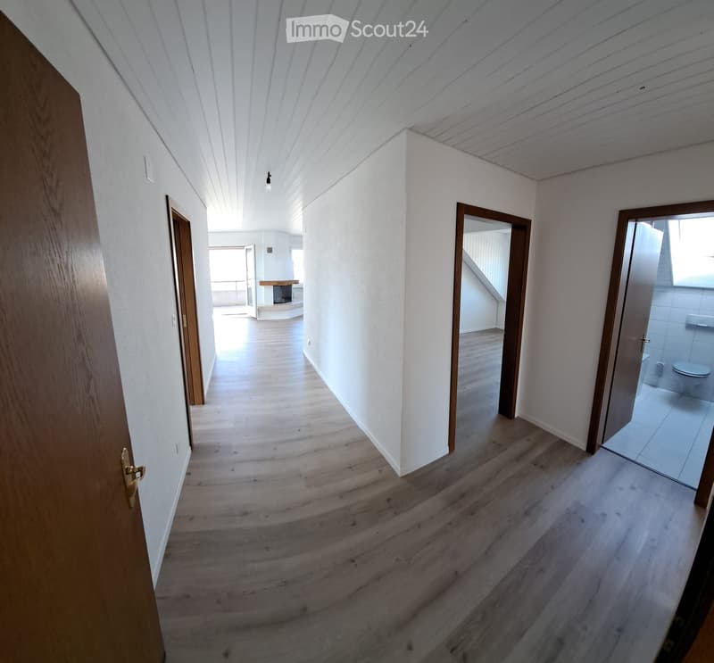 Empty hallway with wooden flooring, white walls, and several doors leading to different rooms, including a bathroom and a living area.