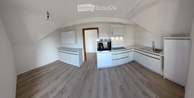Modern kitchen with white cabinets, wooden flooring, stainless steel sink, and oven. The space is well-lit with recessed lighting.