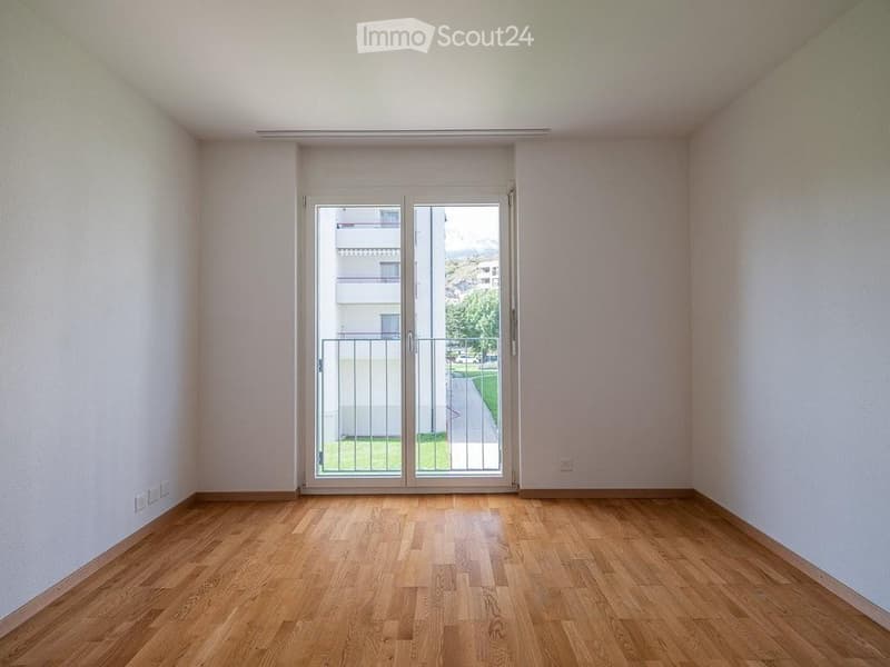 Empty room with wooden flooring, white walls, and a large sliding glass door leading to a balcony or outdoor area.