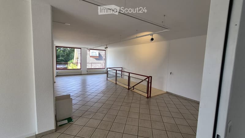 Empty room with tiled floor, white walls, and a staircase leading to another level. There are large windows with a view of the outside, and a small wooden platform at the base of the stairs.