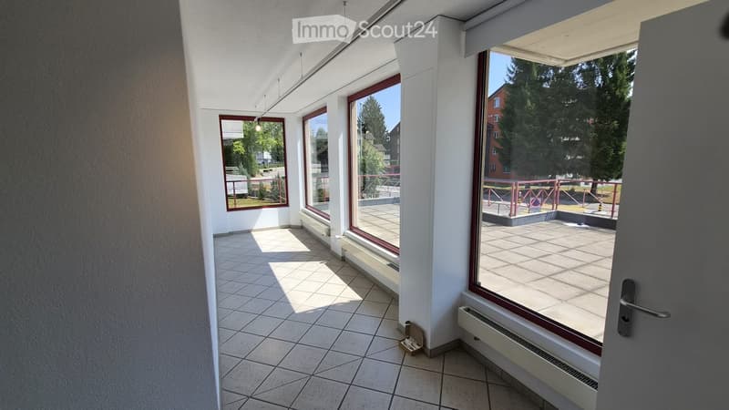 Bright hallway with tiled floor, large windows, and a view of an outdoor area with greenery.