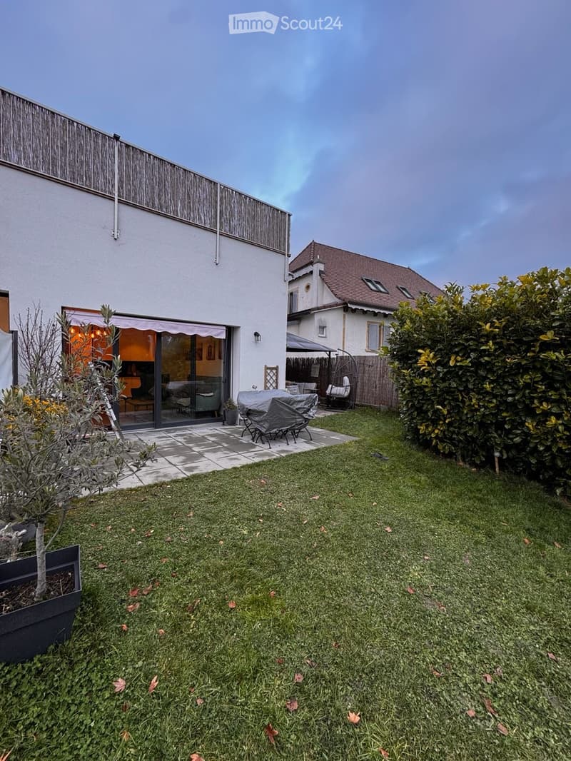 Well-maintained garden with a lawn, patio area, covered seating, and surrounding greenery.