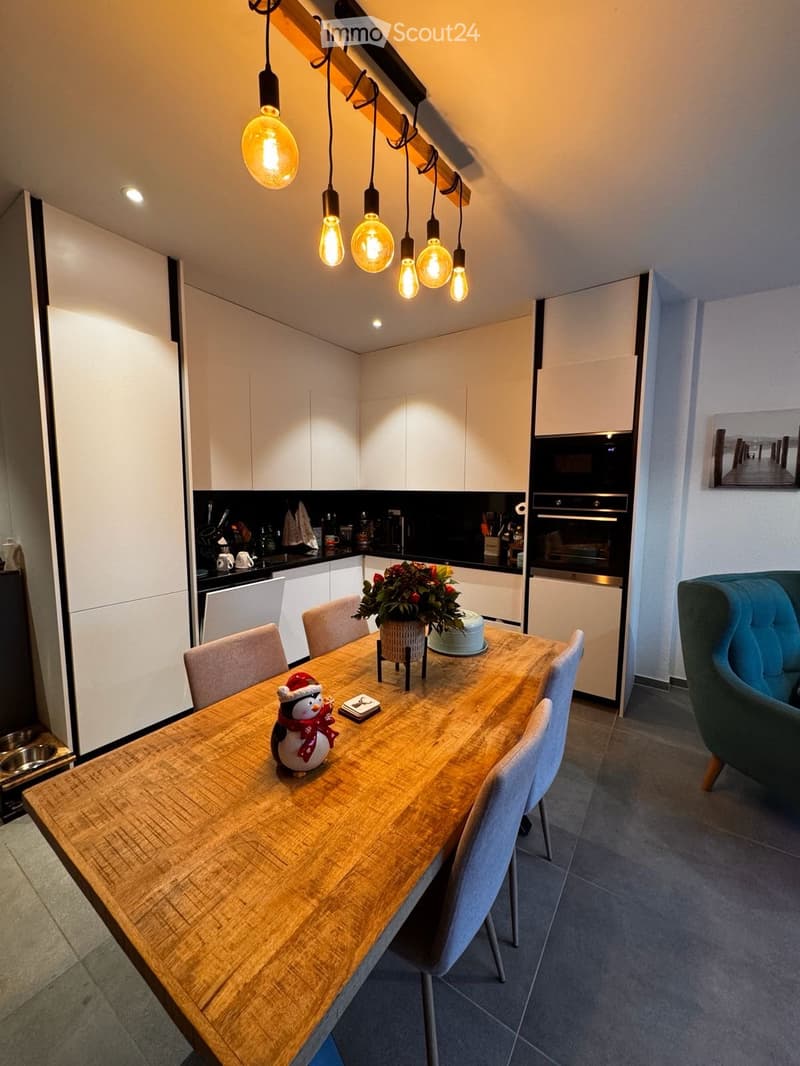 Modern kitchen and dining area with white cabinets, wooden dining table, grey chairs, and a blue sofa in the corner.