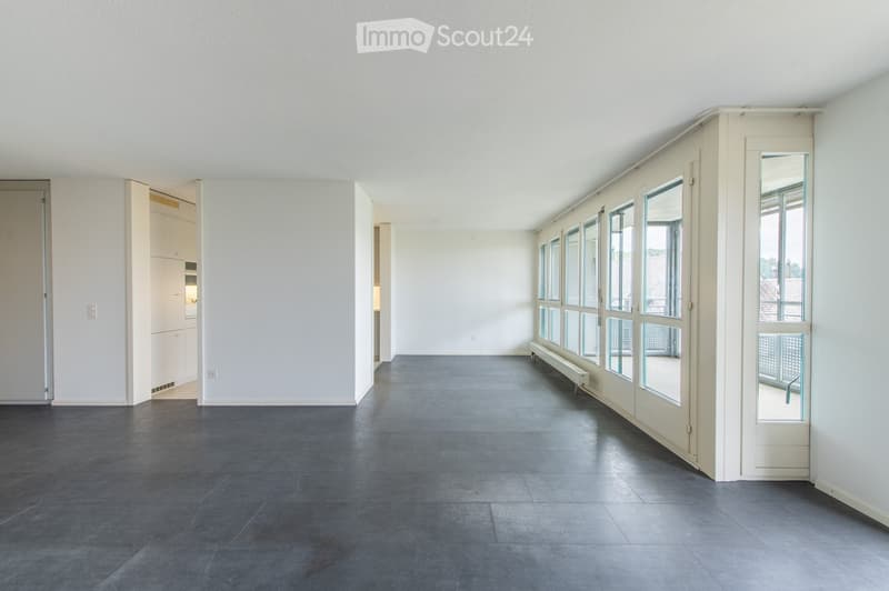 Empty room with grey tiled floor, white walls, large windows, and a bench along the wall.