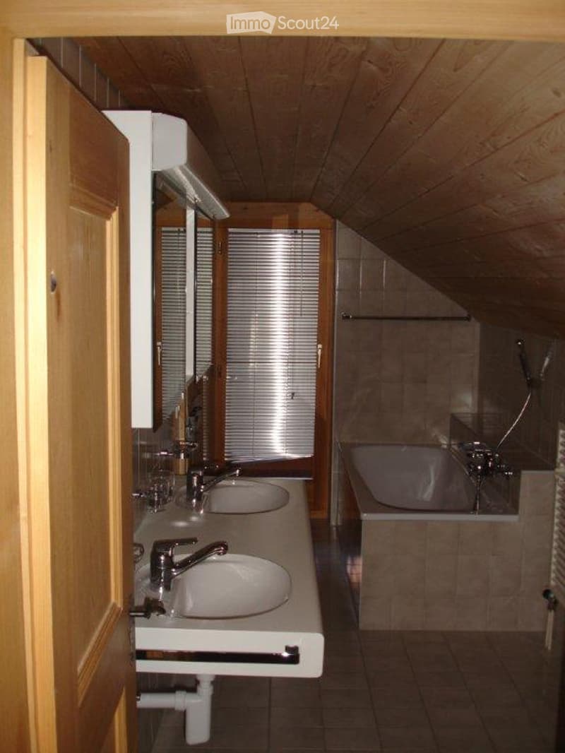 Bathroom with double sinks, mirrors, and a bathtub, featuring wooden ceiling and tiled walls.