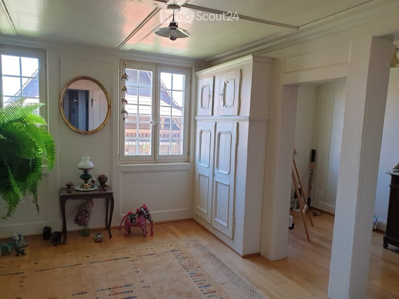 Cozy hallway with wooden flooring, a small table with a lamp, a round mirror, a toy horse, and a decorative rug.
