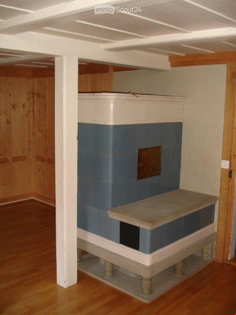 Empty room with wooden flooring, white walls, and a fireplace with blue tiles and a stone bench.