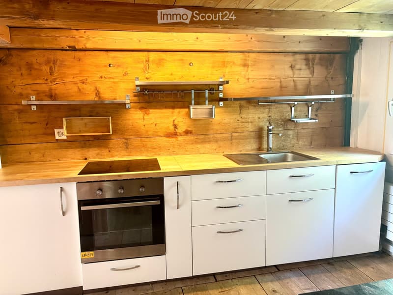 Modern kitchen with white cabinets, stainless steel oven, sink, and faucet, wooden countertops, and wooden walls.
