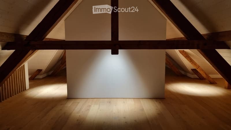 Empty attic space with wooden beams, white walls, and wooden flooring. Natural light streams in from the sides, highlighting the clean and minimalist design.