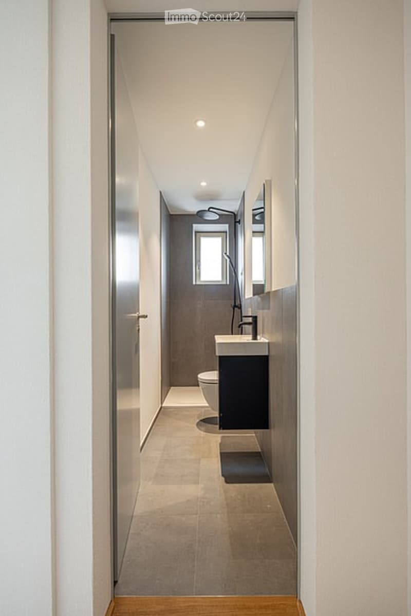 Modern, narrow hallway leading to a contemporary bathroom with sleek fixtures, a floating vanity, and a large mirror.