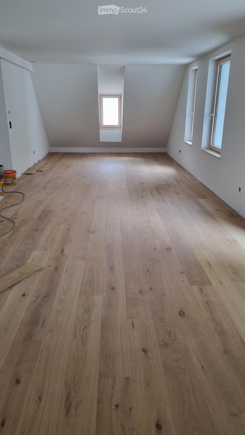 Empty room with wooden flooring and white walls, featuring multiple windows and a small doorway.