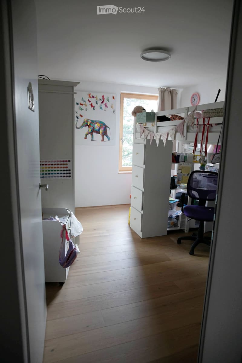 A well-lit bedroom with wooden flooring, a bunk bed, a purple office chair, a grey cabinet, and a storage unit. The walls are decorated with colorful artwork, including butterflies and an elephant.