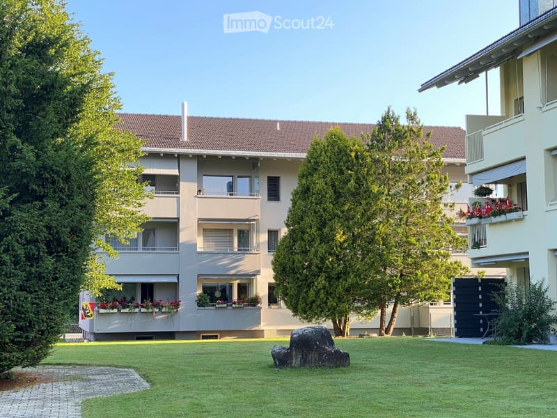 A multi-story residential building with balconies, surrounded by greenery and a well-maintained lawn.