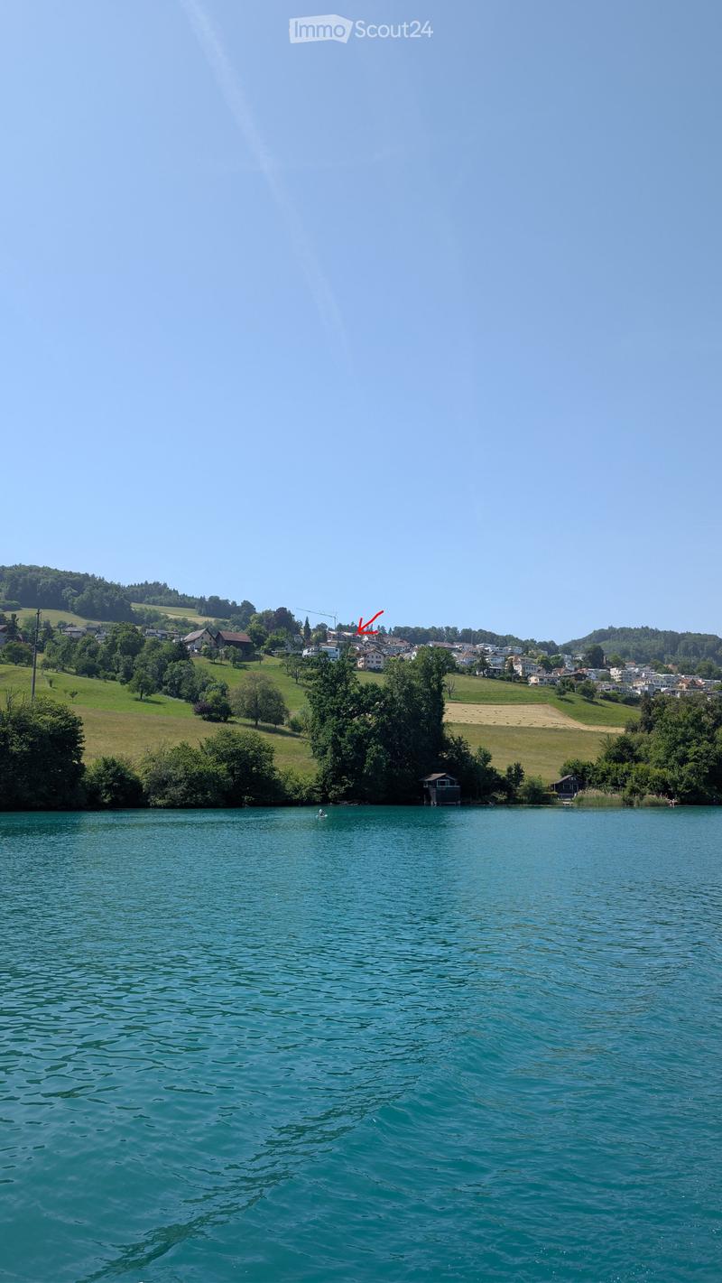 A serene lake surrounded by green hills and scattered houses, with a small boat visible on the water.